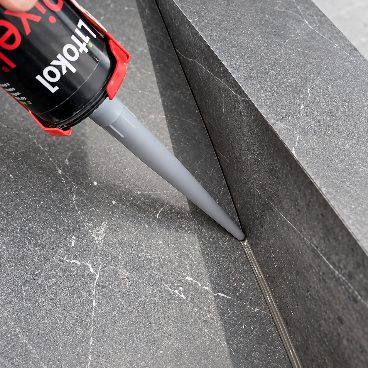 Litokol Pixel® 3D Silikon wird in die Anschlussfuge zwischen grauen Boden- und Sockelfliesen eingebracht.