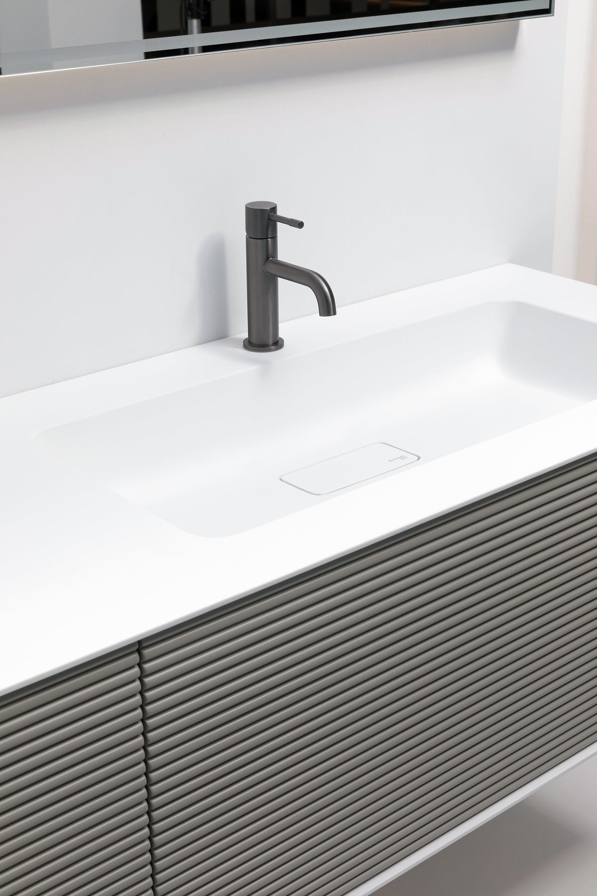 Detalje af Minimal: hvid bordplade med integreret håndvask og armatur over en fint rillet grå front